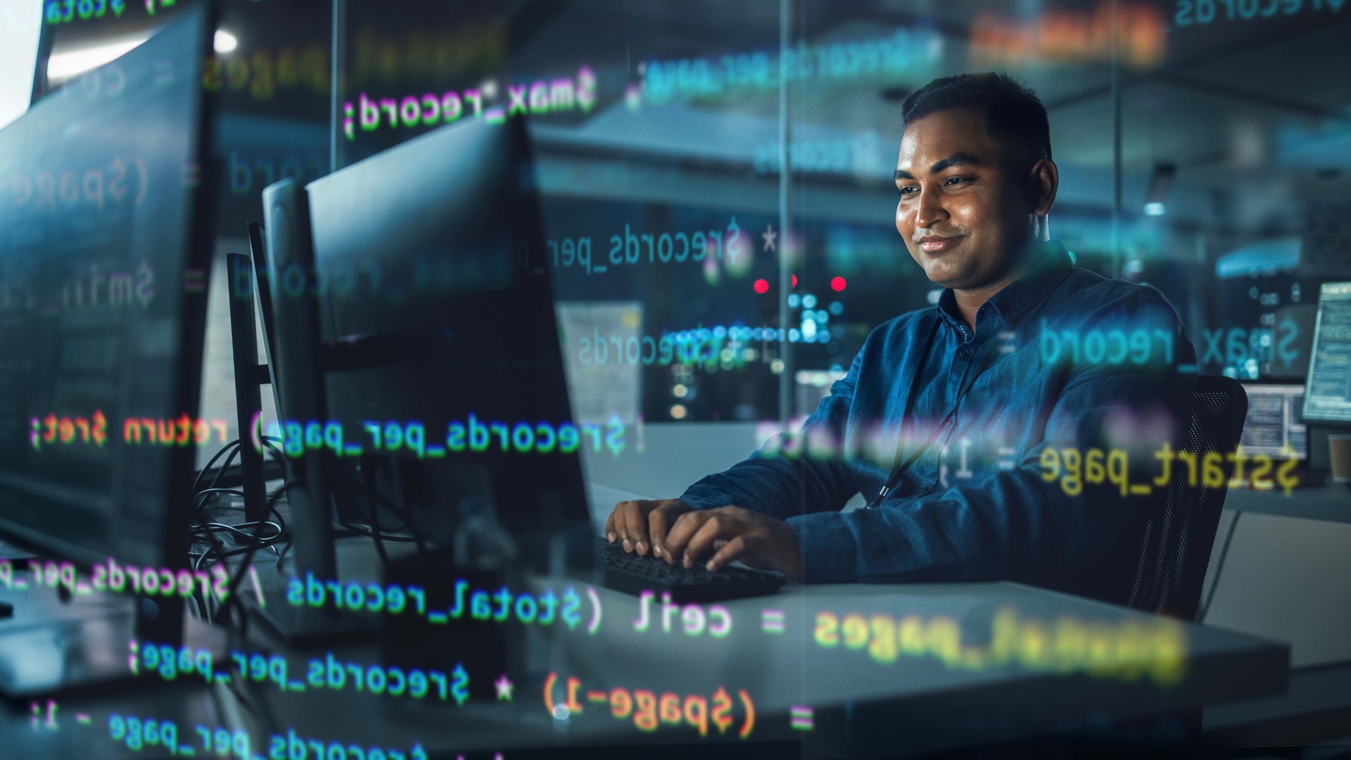 Concept Shot with Visualisation of Running Computer Code on Foreground. Portrait of Handsome Indian Man in Working on Computer at Night in Office. Digital Entrepreneur Creating Modern Software.